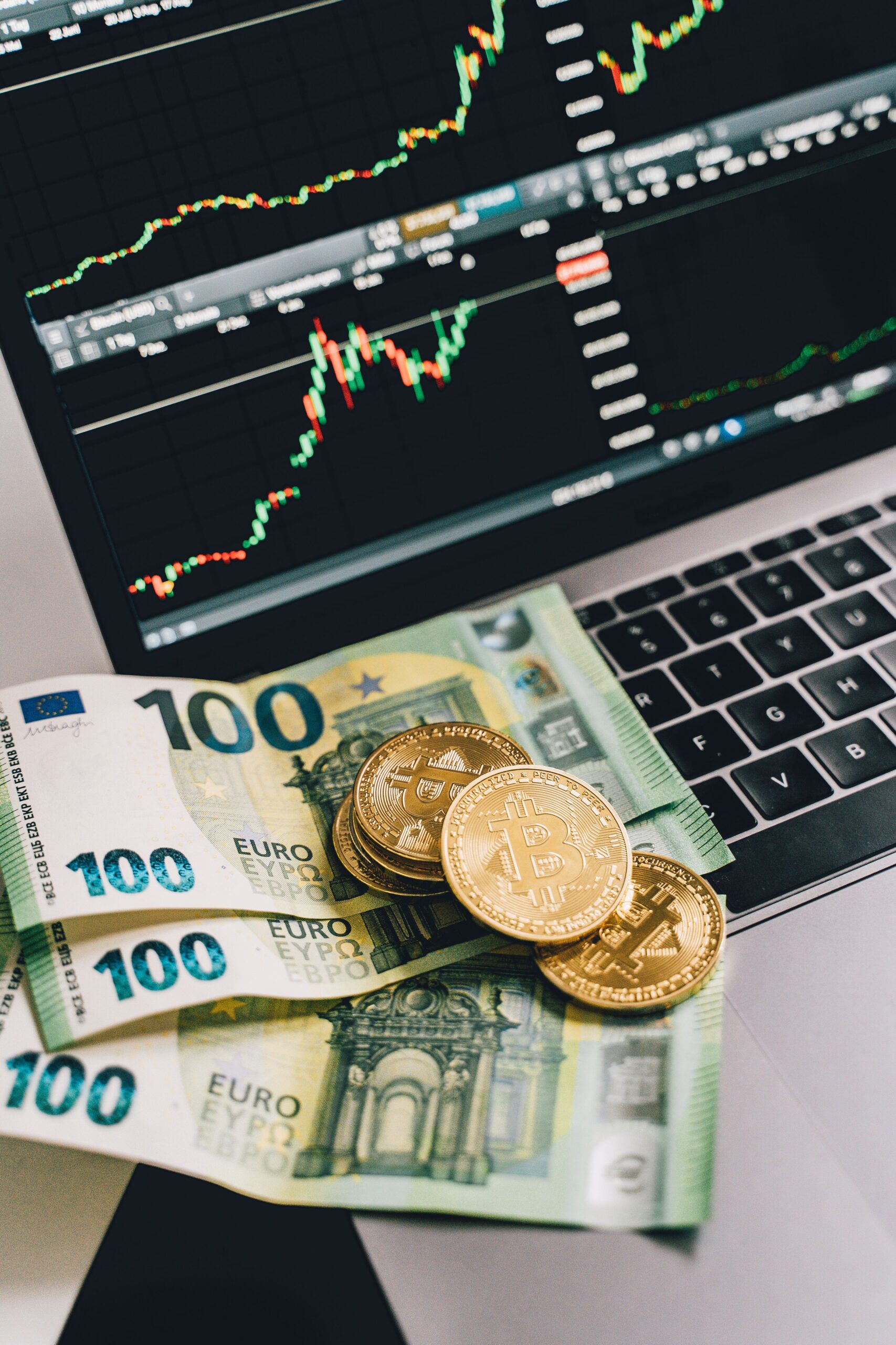 Home Bitcoin coins and Euro notes on a laptop with a stock market graph display, symbolizing modern finance.